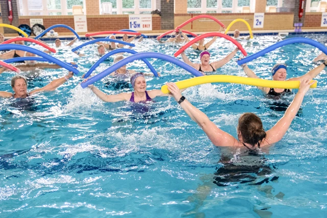 Aqua Mobility class instructor leads participants exercising with dumbbells in a pool.