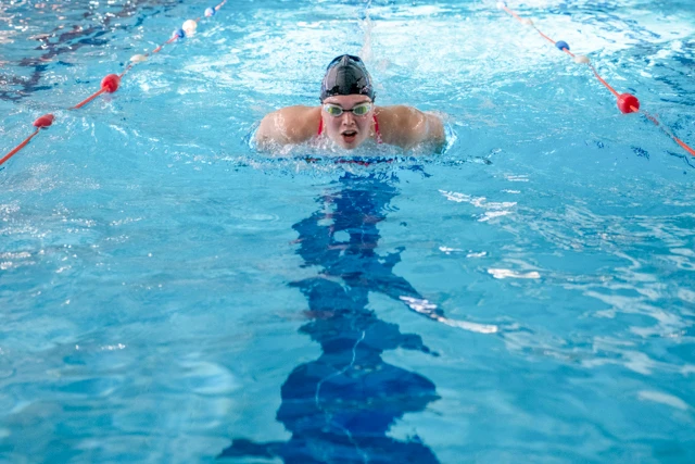 Swim Fitness class image. Picture of a woman in a swimming pool in a swim hat and goggles.