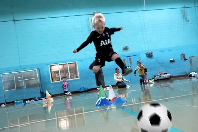 A young child jumps and kicks a ball at tots football