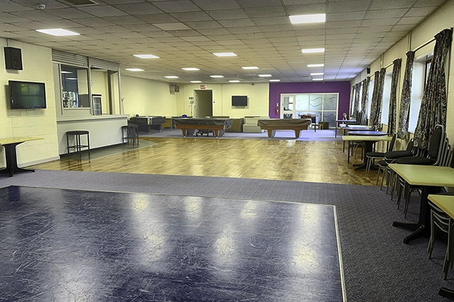 This image shows the community room with multiple pool tables, seating areas, and tables. The room has a large dance floor / open area in the foreground.