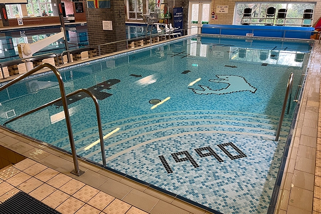 This is a photo of an indoor swimming pool with blue tiled steps that spell out "1990". The pool also has a pixelated dolphin graphic at the bottom.