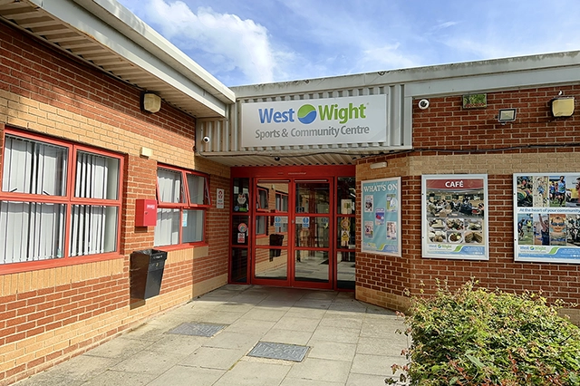 West Wight Sports and Community Centre entrance The West Wight Sports & Community Centre entrance is visible with brick facade and glass doors. Posters for a cafe and community events are displayed on the wall.